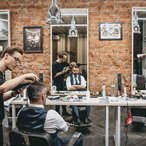 Barber cutting a client's hair in a brick-walled barbershop