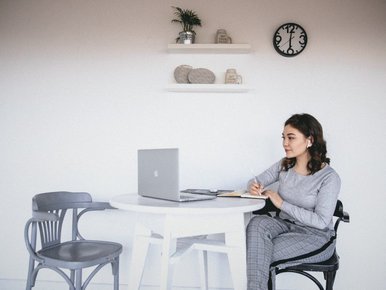 Young woman writing in a notebook beside her laptop at a desk