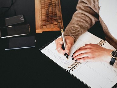 Hands writing in a planner on a desk next to phones