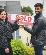 Real estate agent handing house keys to a buyer in front of a sold sign