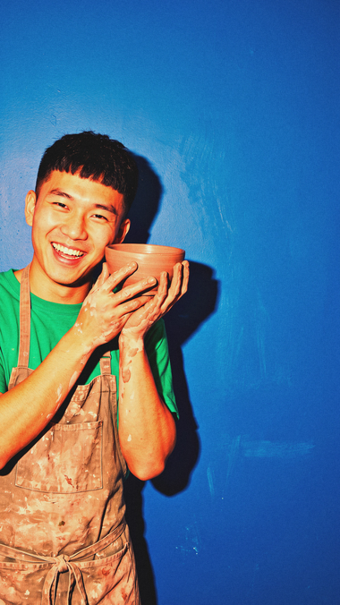 A young man smiles, holding a clay bowl he just made.