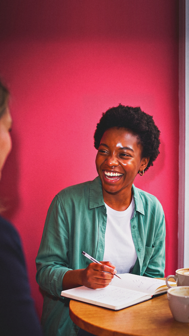 A young woman laughs at something her mentor said over coffee.