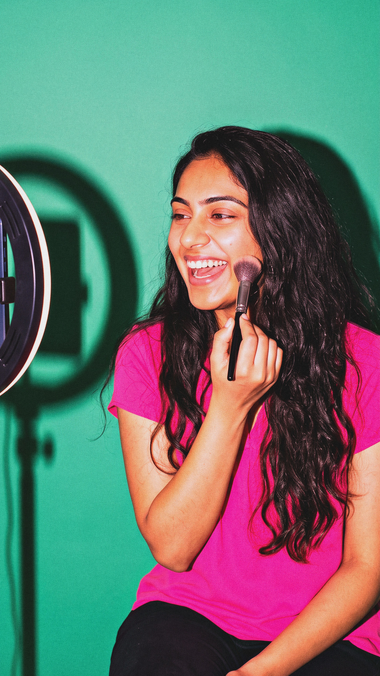 A young woman films her get-ready-with-me routine with a ring light.