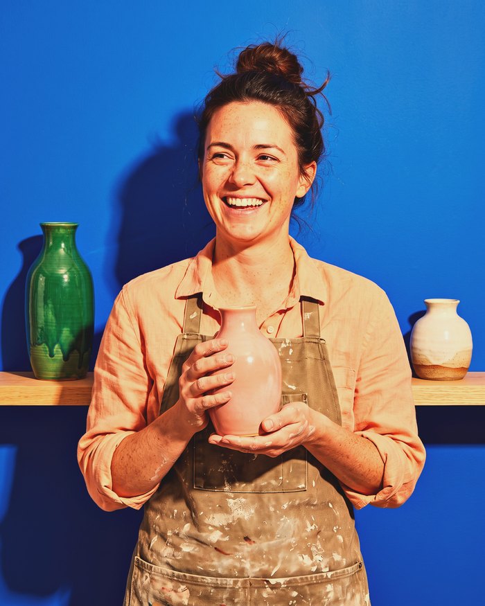 A potter, a laughing woman holding a pink vase.