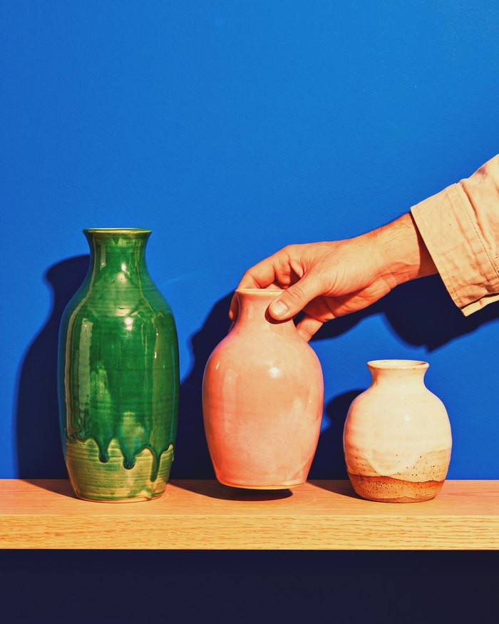Glazed vases and mugs on an oak shelf against a cobalt wall.