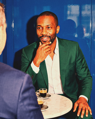A broker leans in to listen to a client over espresso.